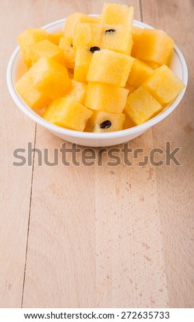 Bite size yellow watermelon fruit in white bowl on wooden cutting board