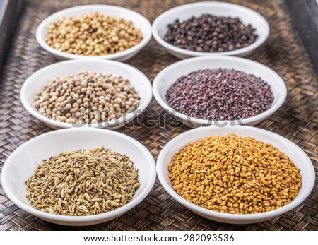 Coriander seed, fenugreek seed, black pepper, white pepper, black mustard seed and cumin seed in white container on wicker surface