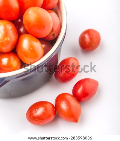 Bite sized red cherry grape tomato in blue pot over white background
