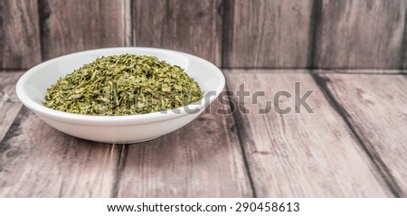 Dried parsley herb in white bowl on weathered wooden background