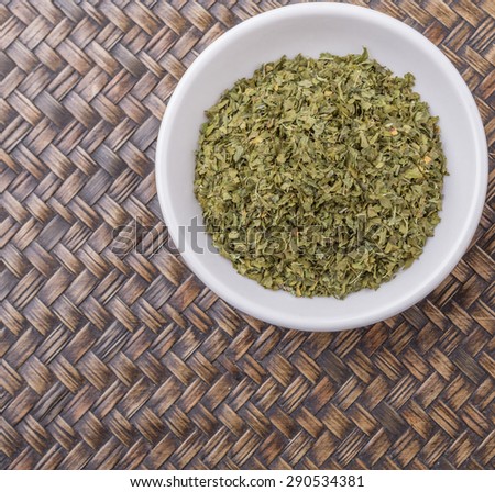 Dried parsley herb in white bowl over wicker background