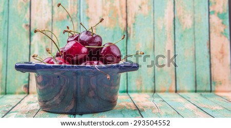 Cherry fruit in a blue pot over weathered light green wooden background