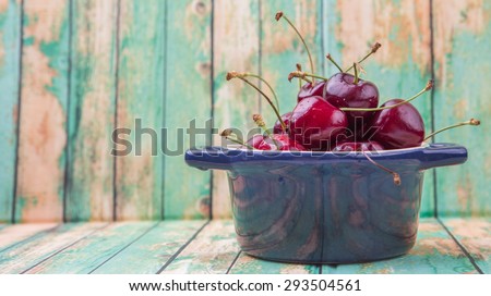 Cherry fruit in a blue pot over weathered light green wooden background