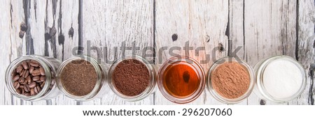 Coffee beans, coffee powder, creamer, cocoa powder, honey and processed tea leaves in a mason jar over weathered wooden background