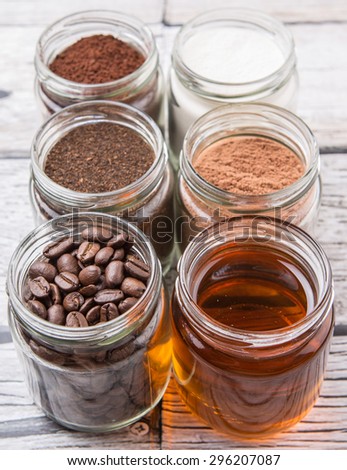 Coffee beans, coffee powder, creamer, cocoa powder, honey and processed tea leaves in a mason jar over weathered wooden background