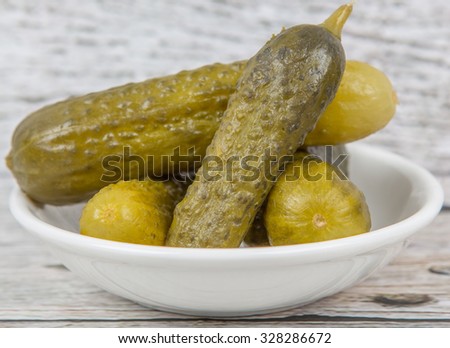 Dill pickles in a white bowl over wooden background