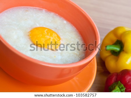 Rice porridge with egg in orange bowl on wood table with paprika.