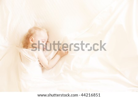a sweet little child sleeping on a white bed sheets, space for text