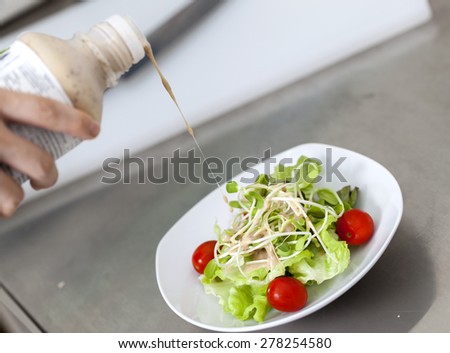 Pouring salad sauce on sunflower sprout salad with small tomato.