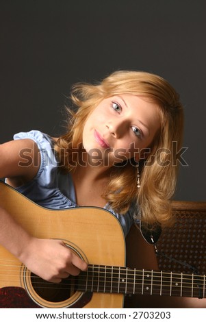 Blond teenage girl wearing blue top and playing guitar
