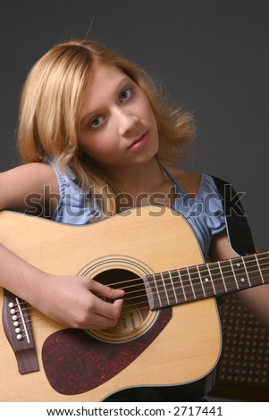 Teenage girl wearing blue top against dark background playing guitar