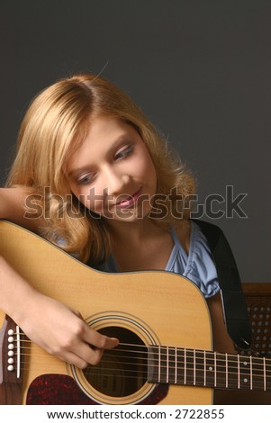 Teenage girl wearing blue top against dark background playing guitar
