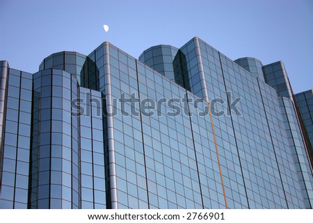 Half moon over Dallas skyline and glass building at sunset