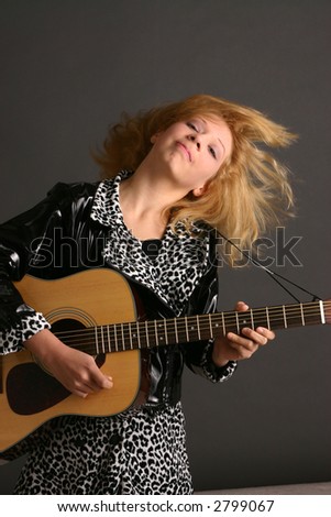 Blond teenage girl wearing punk rock outfit and playing a guitar before dark background