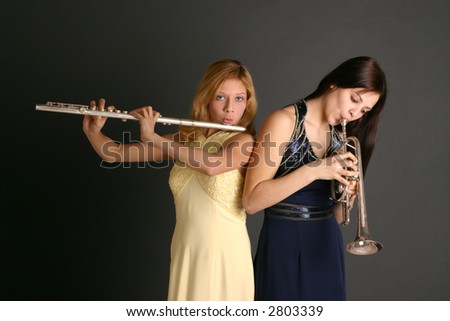 Teenage sisters with flute and trumpet wearing prom dresses against dark background