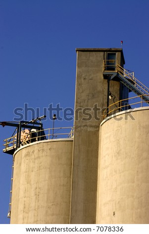 Concrete industrial storage towers against clear blue sky showing railing stairs ladder door hoist illumination