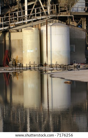 Cylindrical storage tanks and walkways reflected in a water pool at a large concrete plant