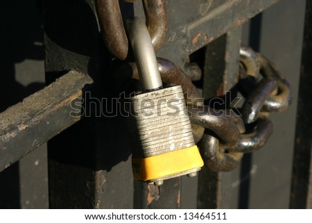Laminated padlock and steel chain secure a steel bar gate