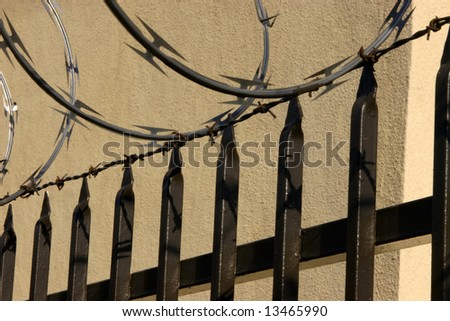 Steel bars razor wire and security fence against beige stucco wall