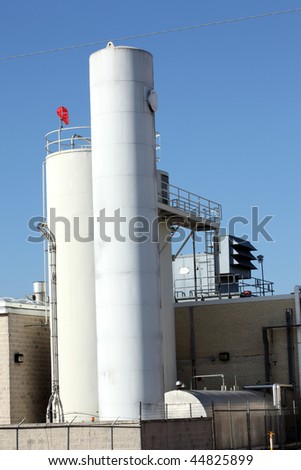 Industrial towers and tanks at a manufacturing plant showing cylindrical towers ladders walkways and air conditioning systems against a blue sky