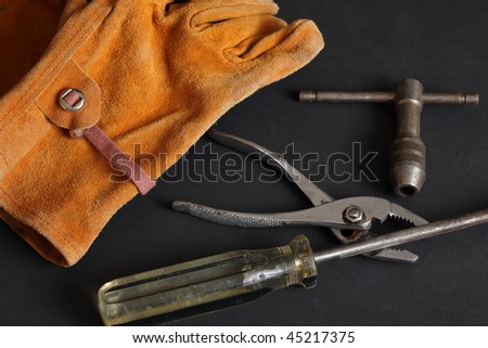 Suede leather work glove battered screw driver pliers and tap handle on a black background