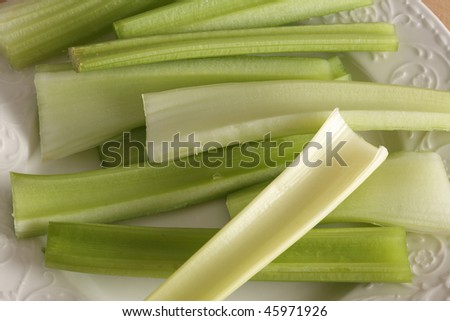 Sticks of fresh celery on a white plate on a wooden cutting board
