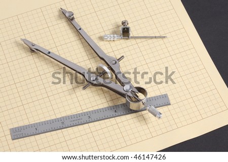 Macro view of mechanical drafting compass and decimal steel scale on yellow grid paper on black background