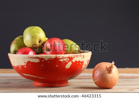 Anjou pears and Gala apples in a chipped painted bowl with a whole yellow onion on a weathered wooden plank deck with black background