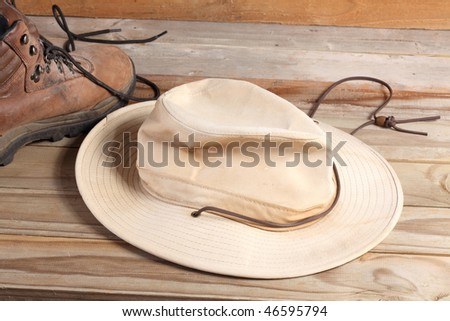 Old fabric outdoor hat with leather strap and leather hiking boot with laces on a weathered wooden plank deck