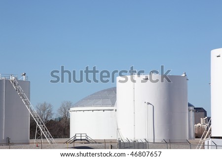 Large white petrochemical storage tanks at a manufacturing plant showing access ladders stairs and walkways and piping