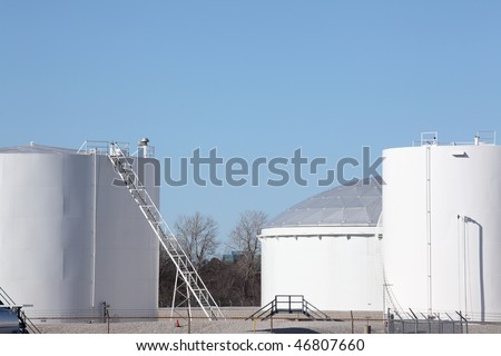 Large white petrochemical storage tanks at a manufacturing plant showing access ladders stairs and walkways and piping