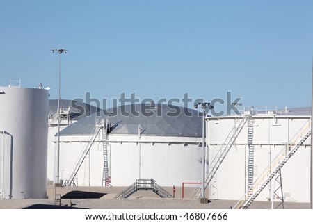 Large white petrochemical storage tanks with domed roofs at a manufacturing plant showing access ladders stairs and walkways and piping