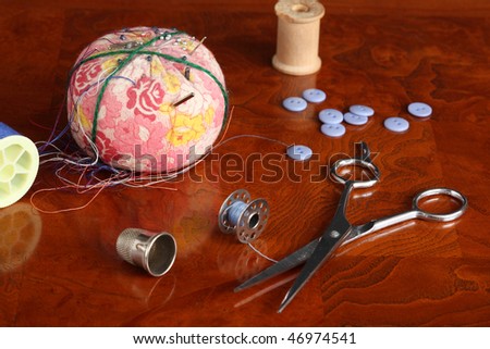 Pincushion needles pins steel bobbin wooden spool blue buttons blue thread plastic spool scissors on a polished wooden surface