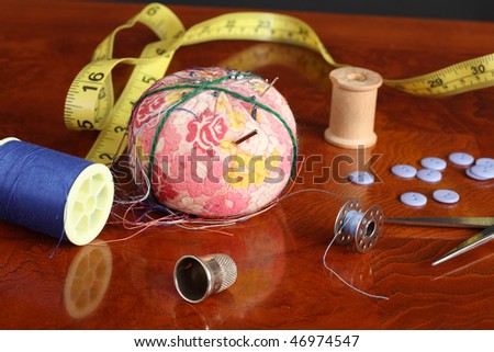 Pincushion needles pins steel bobbin wooden spool blue buttons blue thread plastic spool tape measure showing inches on a polished wooden surface