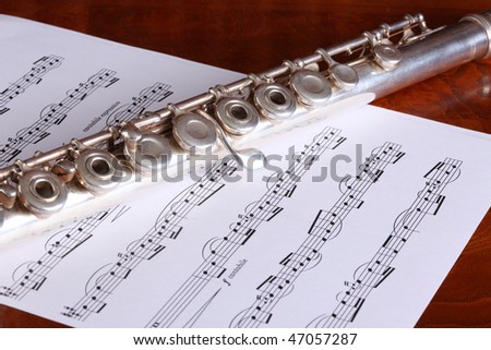 Silver open key flute and classical sheet music resting on a polished wood surface