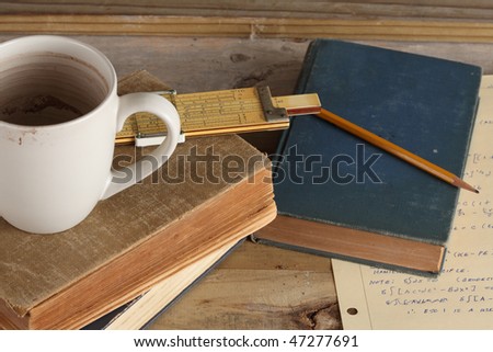 Three worn books with cup slide rule and wooden pencil on a weathered wooden plank deck