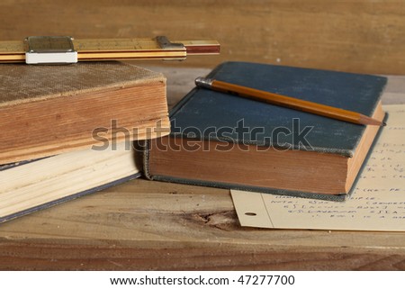 Three worn books with cup slide rule and wooden pencil on a weathered wooden plank deck