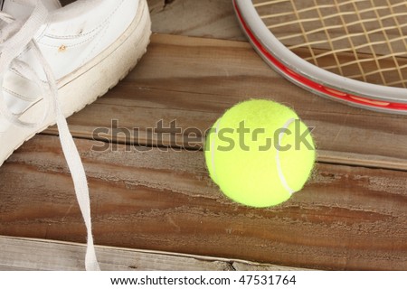 Yellow tennis ball and old white tennis shoe with aluminum racket on a weathered wooden plank deck