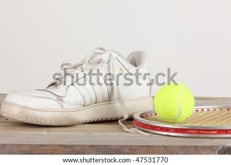 Yellow tennis ball and old white tennis shoe with aluminum racket on a weathered wooden plank deck