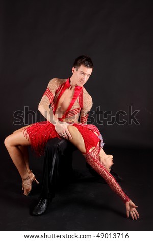 Man and woman ballroom dancers in exotic costumes perform an acrobatic dance against black background