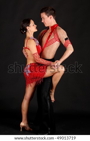 Man and woman ballroom dancers in exotic costumes perform acrobatic dance against black background