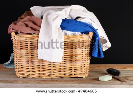 Wicker basket with multi-colored laundry soap and brush on a weathered wooden plank deck before a black background
