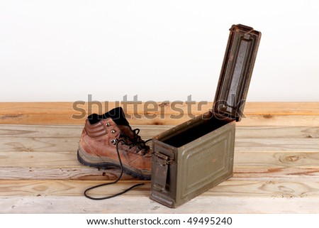 World War Two metal container for thirty caliber ammunition and hiking boot on a weathered wooden plank deck against white background