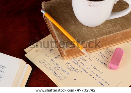 Old college physics text book and class notes with coffee cup and yellow pencil on a polished wooden table top