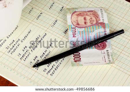 Coffee cup with general ledger sheet showing journal entries and black ballpoint pen with Italian one thousand lire bank note