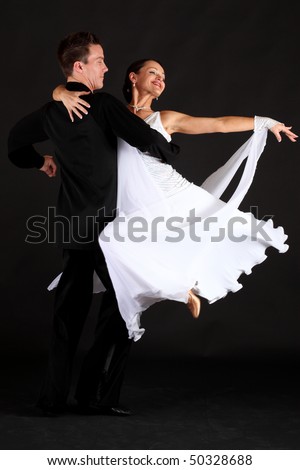 Competition ballroom dancers in formal black and white costumes against black background
