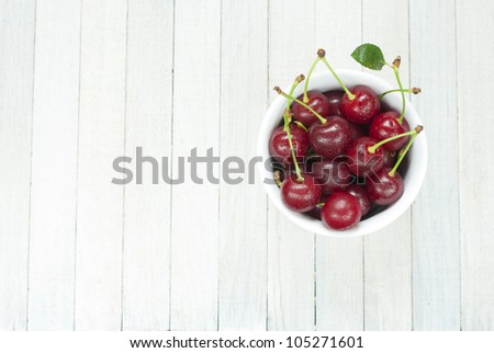 sour cherries in china dish on white wooden table, directly above