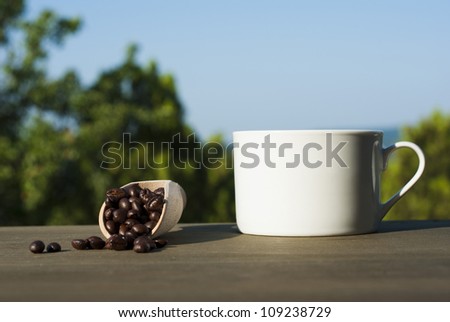 cup of coffee and coffee beans on wooden table in garden