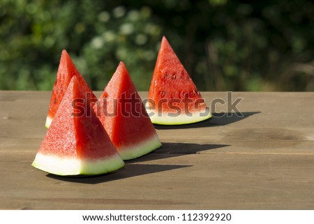 slices of watermelon on wooden table, mediterranean garden background