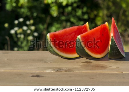 slices of watermelon on wooden table, mediterranean garden background